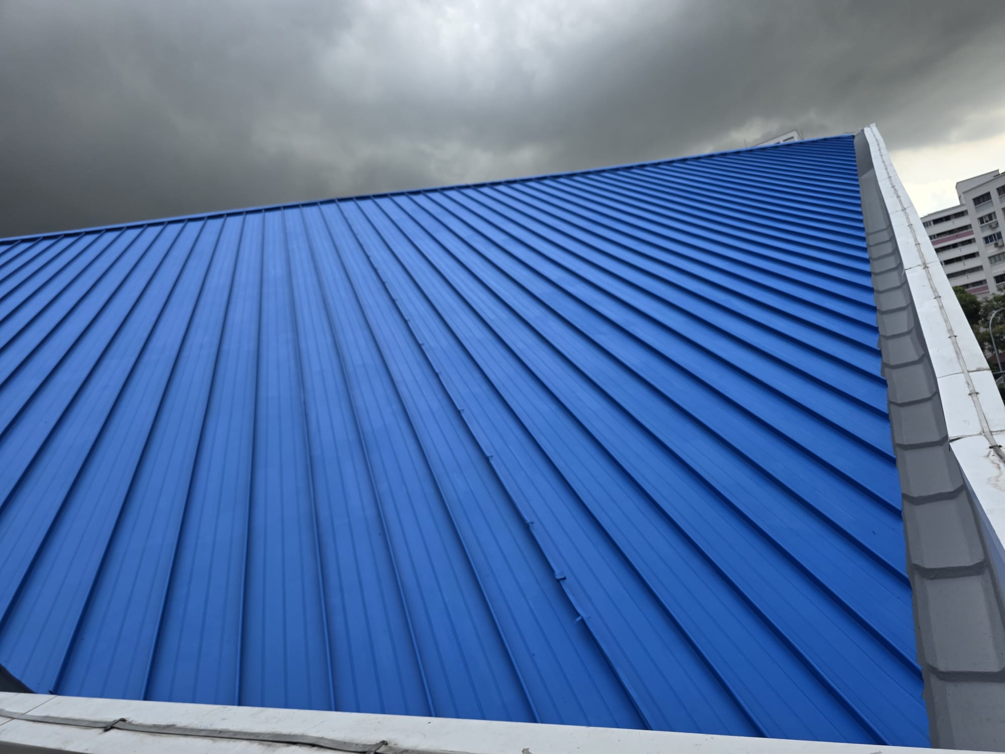 Newly recoated blue metal roof against a dark stormy Singapore sky — Shieldguard waterproofing contractor project